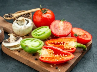 Warzywa: papryka, pomidory i pieczarki na desce do krojenia
