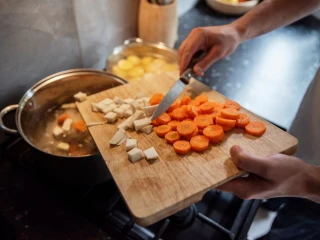 Mężczyzna dodaje pokrojone warzywa do gotującej się zupy