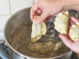 Kobieta wrzuca pierogi do garnka z gotującą wodą