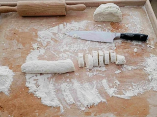 Na stolnicy leży kulka ciasta, ciasto w formie wałka i nóż