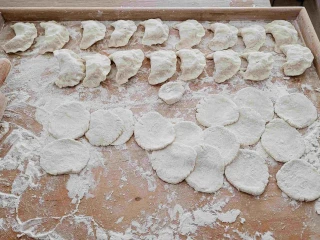 Na stolnicy leżą ulepione pierogi i rozwałkowane kawałki ciasta, obok leży wałek