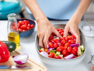 Kobieta miesza rękoma warzywa: cukinię, paprykę i pomidorki z oliwą