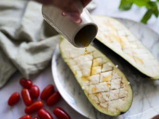 Kobieta wylewa oliwę na połówkę bakłażana