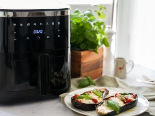 Upieczony bakłażan z pomidorkami i mozzarellą na białym talerzu stojącym obok Air Fryera Bosch Serie 6