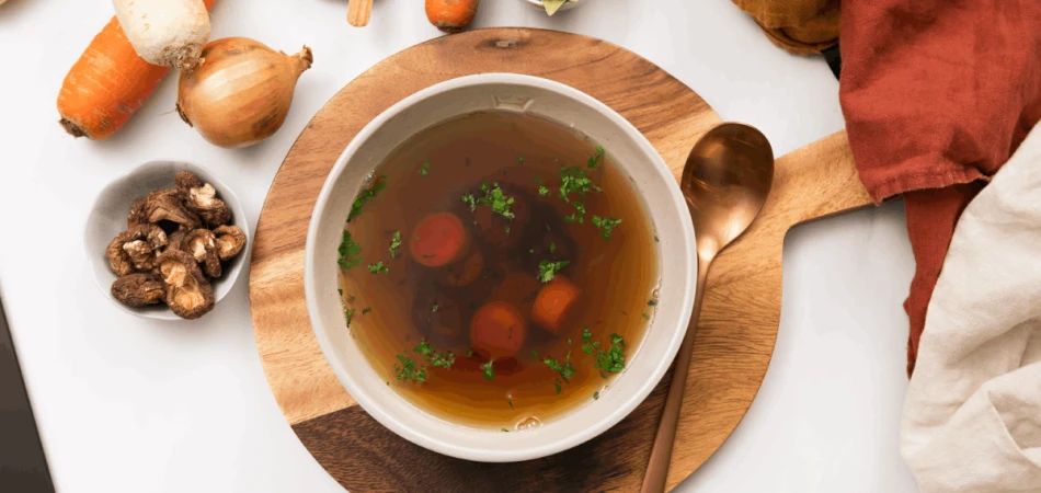 bulion wegański z grzybami i tymiankiem w miseczce na drewnianej desce