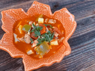 Bogracz z kluseczkami w czarnej misce na drewnianej desce