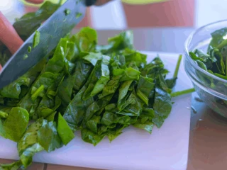 Kobieta krojąca szpinak na białej desce