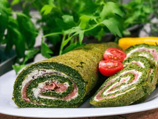 Naleśniki szpinakowe z wędzonym łososiem i serkiem podane na białym talerzu