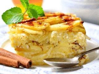 Kawałek zapiekanki makaronowej z jabłkami podany na talerzu i przystrojony listkiem mięty