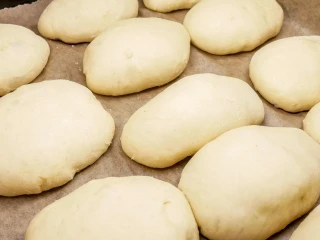 Surowe, wyrośnięte jagodzianki ułożone na papierze do pieczenia, gotowe do wstawienia do piekarnika