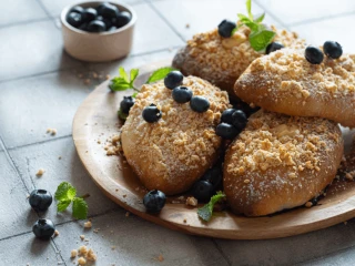 Upieczone jagodzianki z kruszonką na drewnianym talerzu przystrojone jagodami i listkami mięty