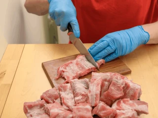 Kobieta w niebieskich rękawiczkach kroi żeberka na kawałki