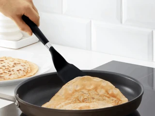 Kobieta przekłada na drugą stronę smażonego naleśnika