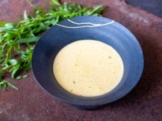 Sos berneński podany w granatowej misce, obok leżą gałązki estragon