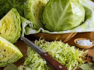 Pokrojona kapusta na drewnianej desce, obok leżą całe główki kapusty