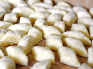 Surowe kluski leniwe pokrojone w romby, ułożone na drewnianej stolnicy przed gotowaniem