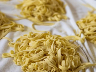 Gniazda świeżo przygotowanego, surowego makaronu tagliatelle ułożone na białej ściereczce, gotowe do gotowania