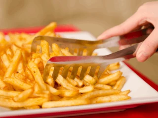 Kobieta przekłada upieczone frytki na talerz