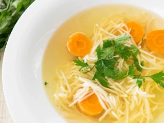 Rosół z makaronem, marchewką i natką pietruszki w białym talerzu