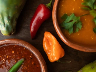 Kompozycja składników do zupy meksykańskiej: miseczki z czerwonym sosem, pomarańczowym sosem chili, zieloną papają, czerwonymi papryczkami i świeżą kolendrą na ciemnym tle