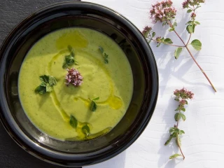 Czarna misa z gładką zupą krem z brokułów polaną oliwą i udekorowana oregano oraz gałązką tymianku na białym tle