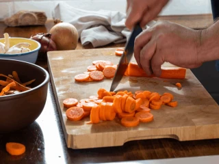 Mężczyzna kroi marchewkę na drewnianej desce