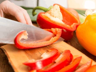 Kobieta kroi czerwoną paprykę na drewnianej desce