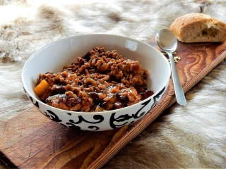 Miseczka z chili con carne -gęste danie z mięsa mielonego, fasoli, warzyw i sosu, podana na drewnianej desce z kromką chleba i łyżką