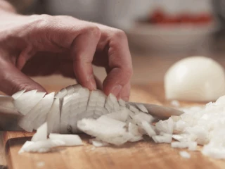 Dłonie krojące drobno cebulę na drewnianej desce