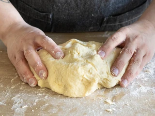 Dłonie zagniatające ciasto na pierogi na usypanej mąką stolnicy