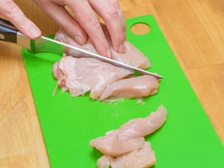 Kobieta kroi pierś z kurczaka na zielonej desce