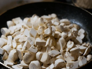 Patelnia wypełniona pokrojonymi w kawałki pieczarkami, przygotowanymi do smażenia