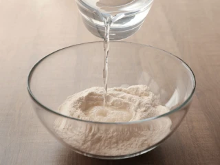 Woda wlewana do miski z mąką i suchymi drożdżami