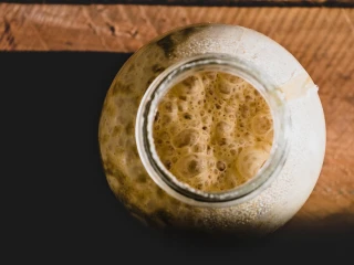 Spieniony zakwas w słoiku na drewnianym blacie, widok z góry