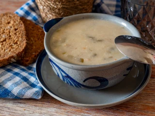 Zupa zalewajka w ceramicznej misce z niebieskim zdobieniem, obok ciemne pieczywo i ścierka z niebieskim wzorem