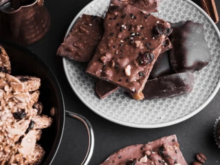 Ciasto blok czekoladowy w kilku kawałkach na jasnym talerzu postawionym na ciemnym blacie, obok inne ciastka