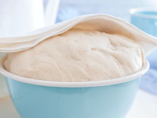 Ciasto na pizzę w niebieskiej misce przykryte ściereczką