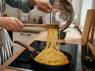 Przekładanie ugotowanego makaronu na patelnie z pozostałymi składnikami
