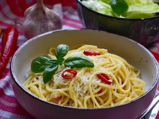 Makaron spaghetti z ostrą czerwoną papryką, startym parmezanem i bazylią w jasnej misce na czerwono-białym obrusie