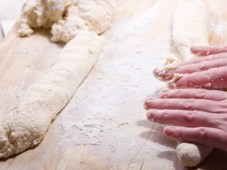 Zbliżenie na ręce kobiety formującej wałek z ciasta na kopytka