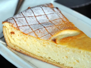 Zbliżenie na kawałek sernika na kruchym spodzie, posypany cukrem pudrem