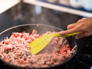 Zbliżenie na rękę kobiety mieszającą mięso mielone na patelni