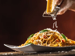 Zbliżenie na talerz ze spaghetti bolognese i ścierany nad nim parmezan