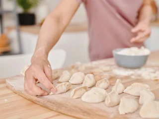 Osoba układa surowe pierogi na stolnicy