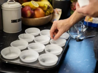 Zbliżenie na mężczyznę wkładającego papilotki do formy do muffinek