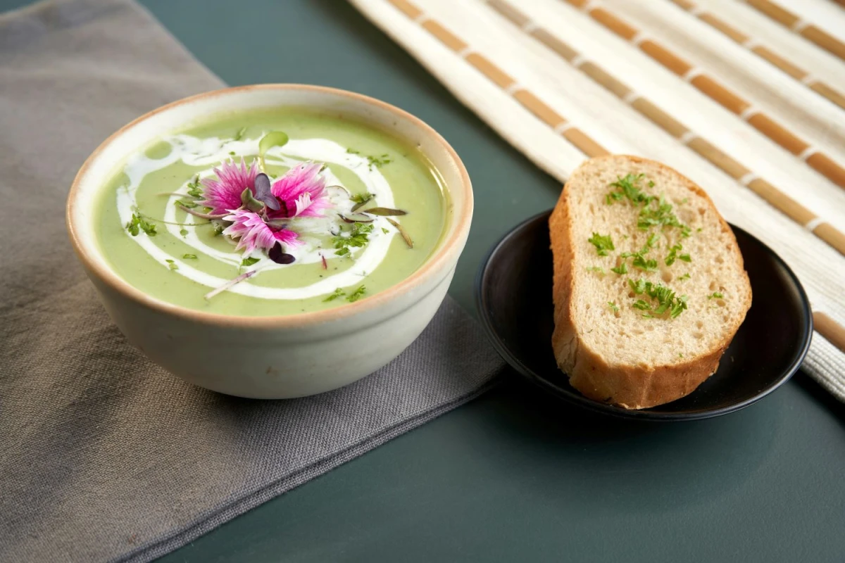 Zielona zupa krem w misce, obok leży kromka chleba.