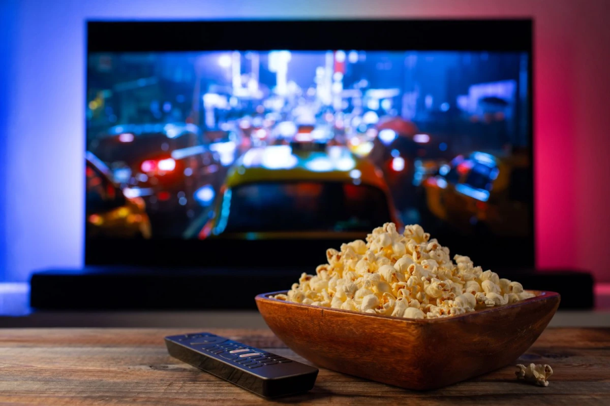 Duża miska pełna popcornu ustawiona przed rozmytym ekranem telewizora w domowym wnętrzu. 