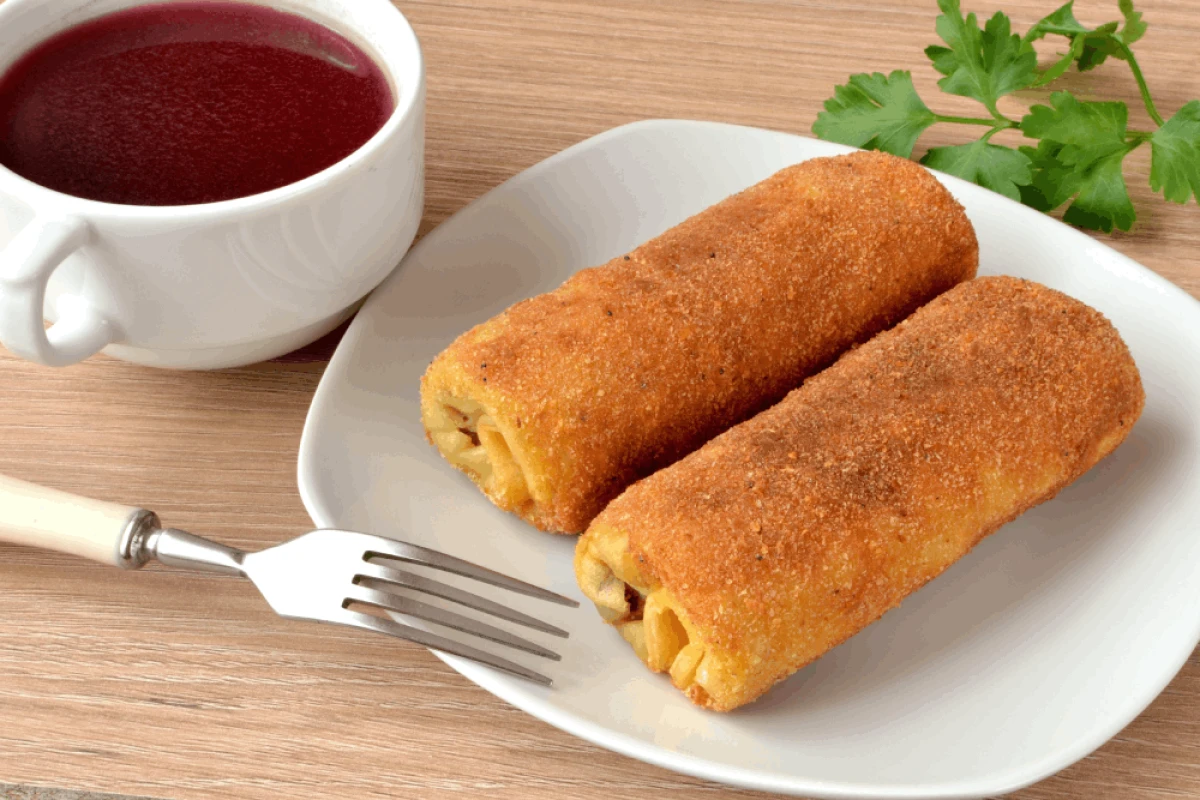 Dwa usmażone krokiety podane na białym talerzu, obok barszcz czerwony w misce