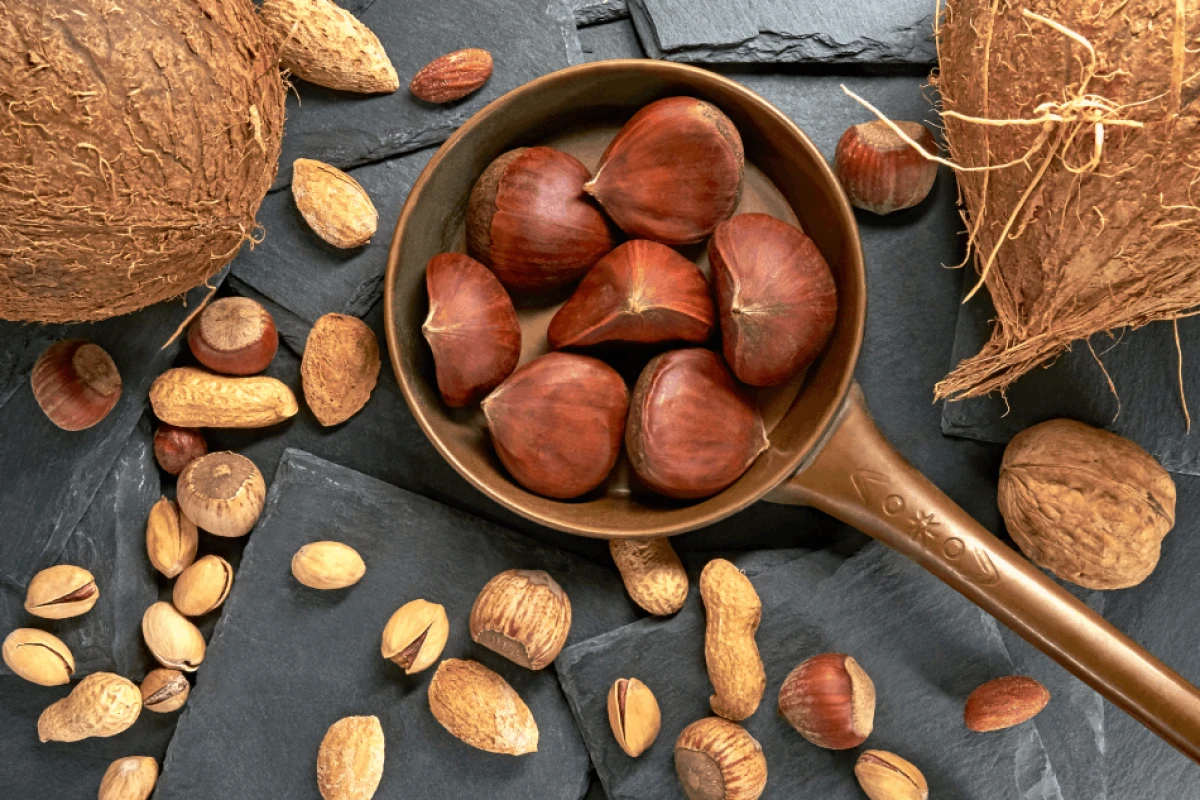 Kasztany jadalne w miedzianym rondelku wśród różnego rodzaju orzechów