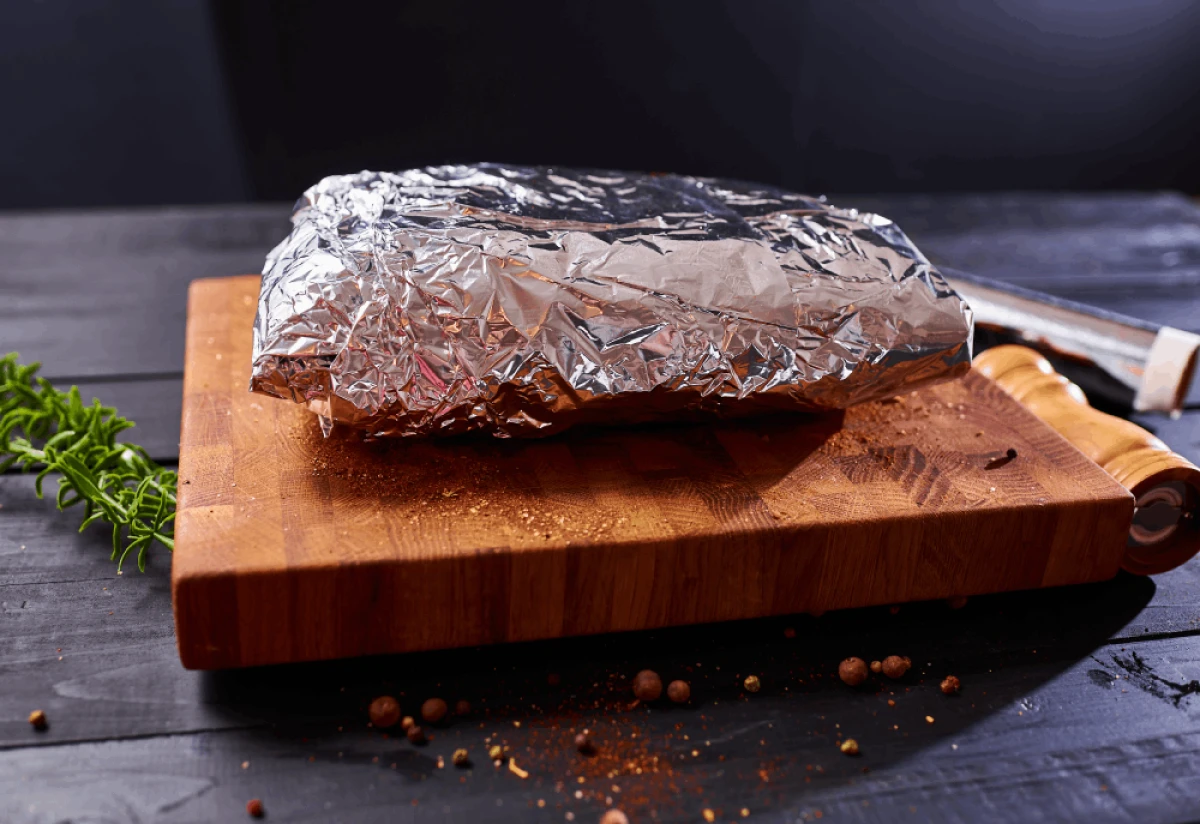 Kawałek mięsa zawinięty w folię aluminiową leży na drewnianej desce